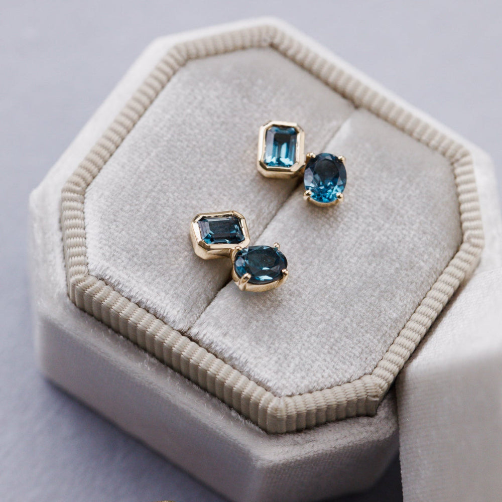 Pair of gold earrings with blue gemstones on a beige cushion