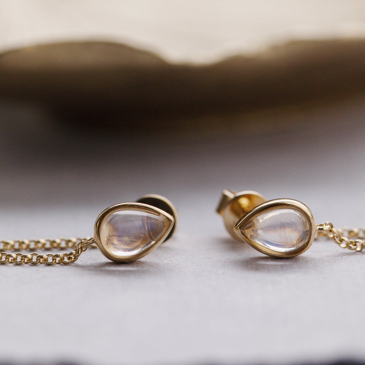 Gold earring with pear-shaped moonstone pendant on a neutral background