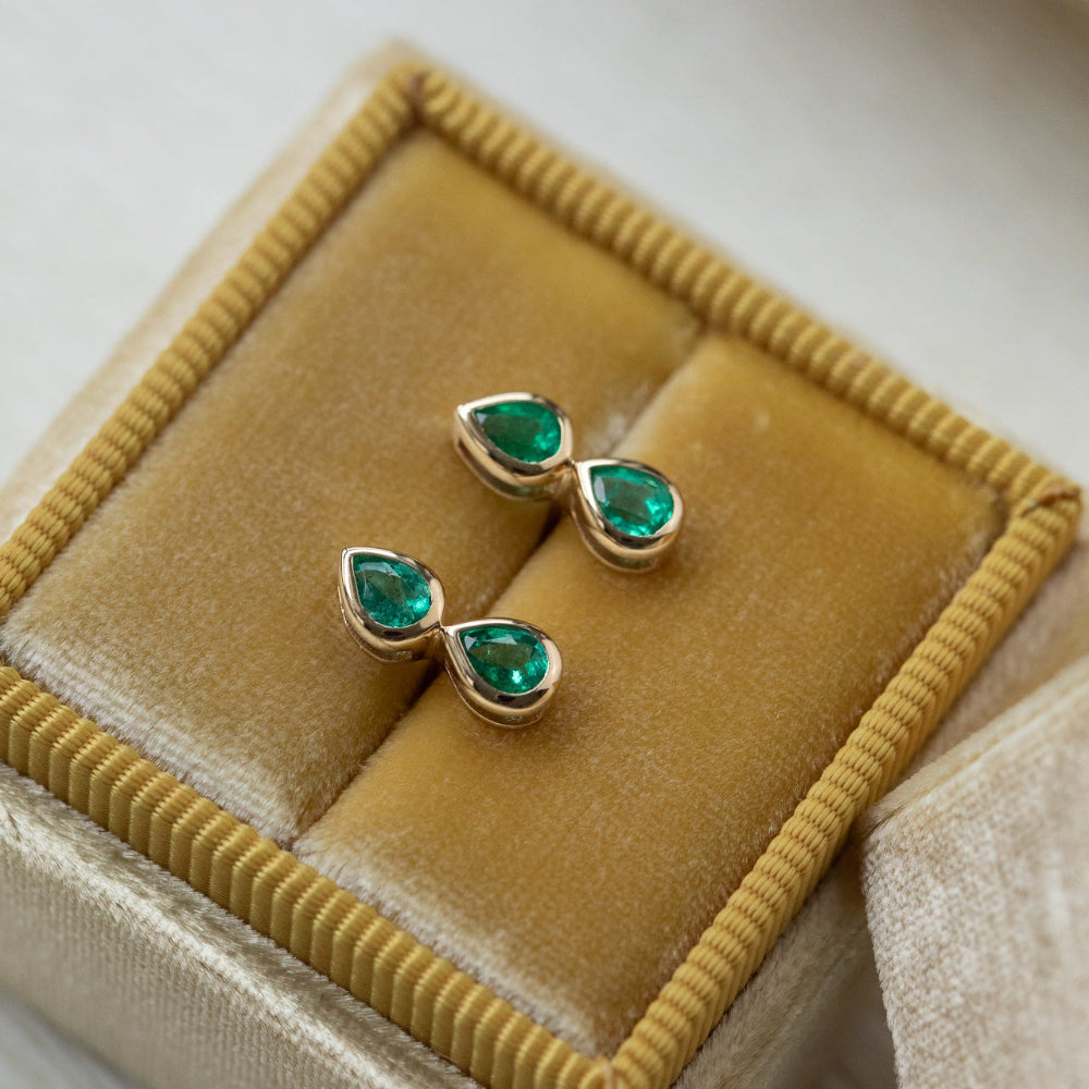 Gold earrings with green gemstones on a beige velvet cushion