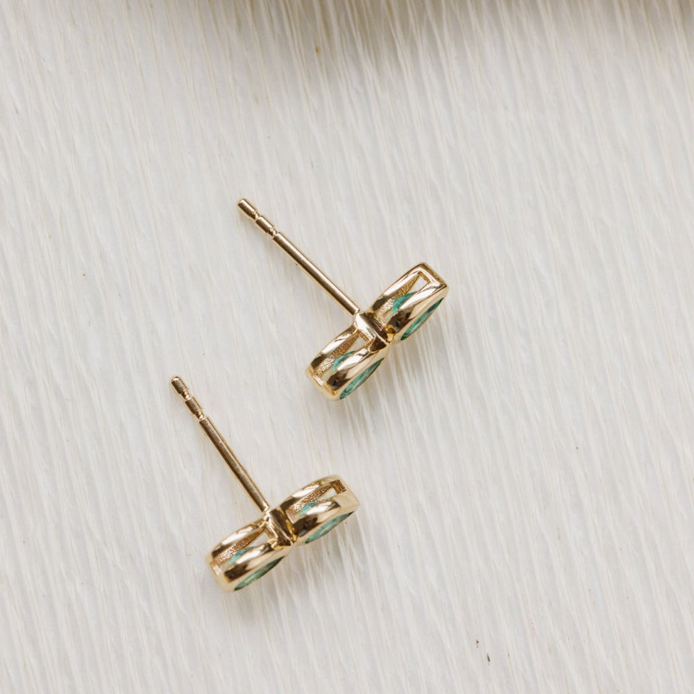 Gold earrings with green gemstones on a light wooden surface