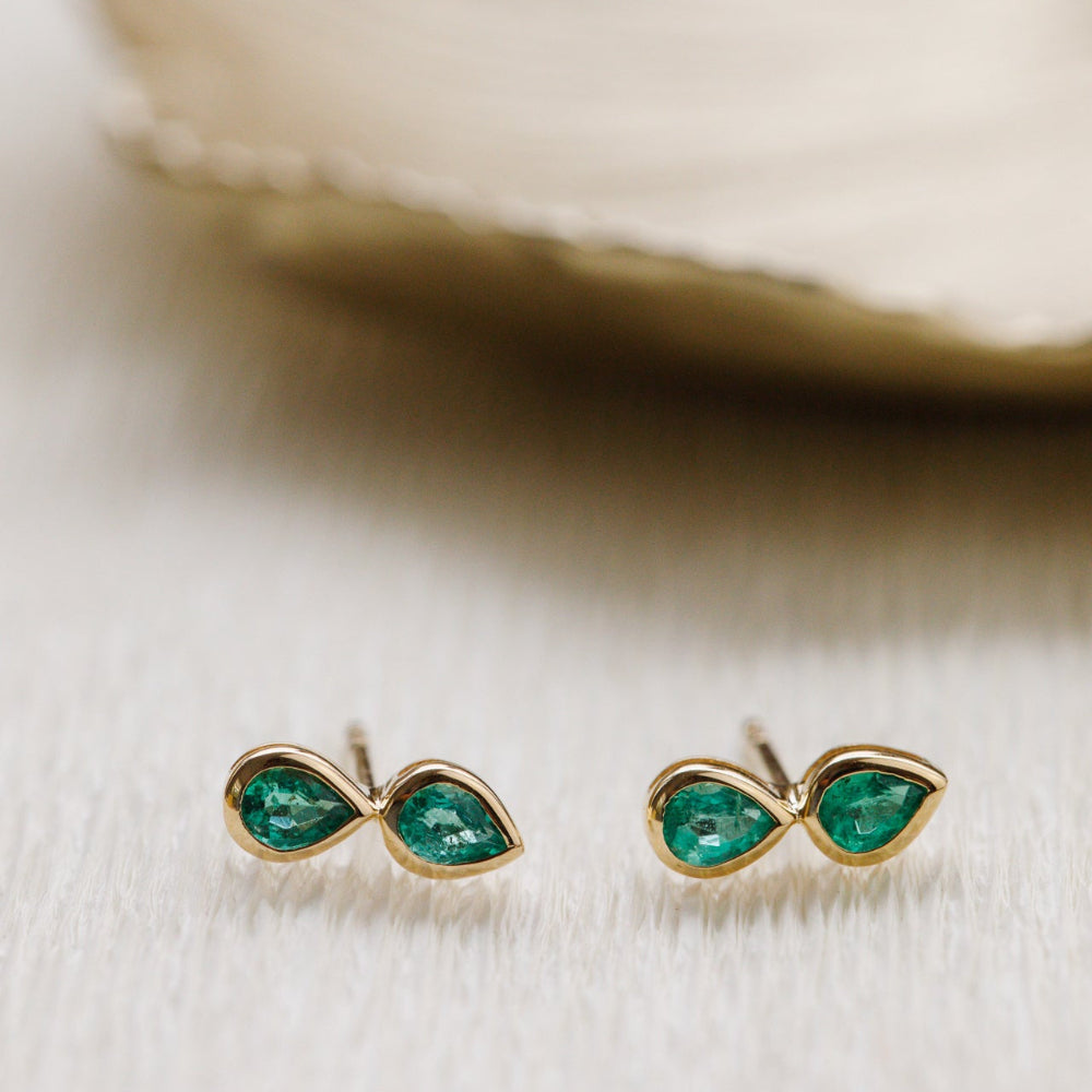Gold earrings with green gemstones on a light background