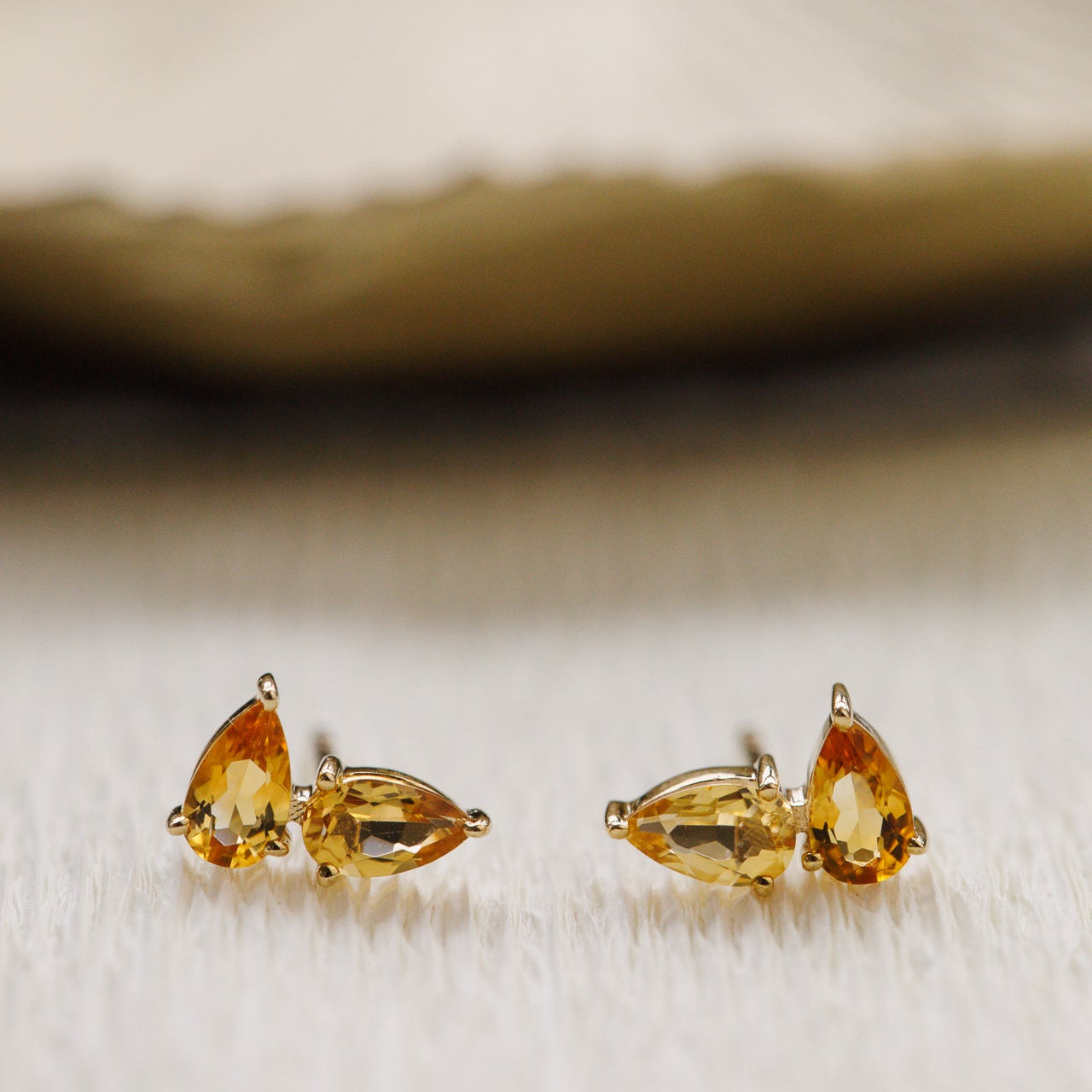 Pair of gold earrings with pear-shaped orange citrine gemstones on a textured beige background