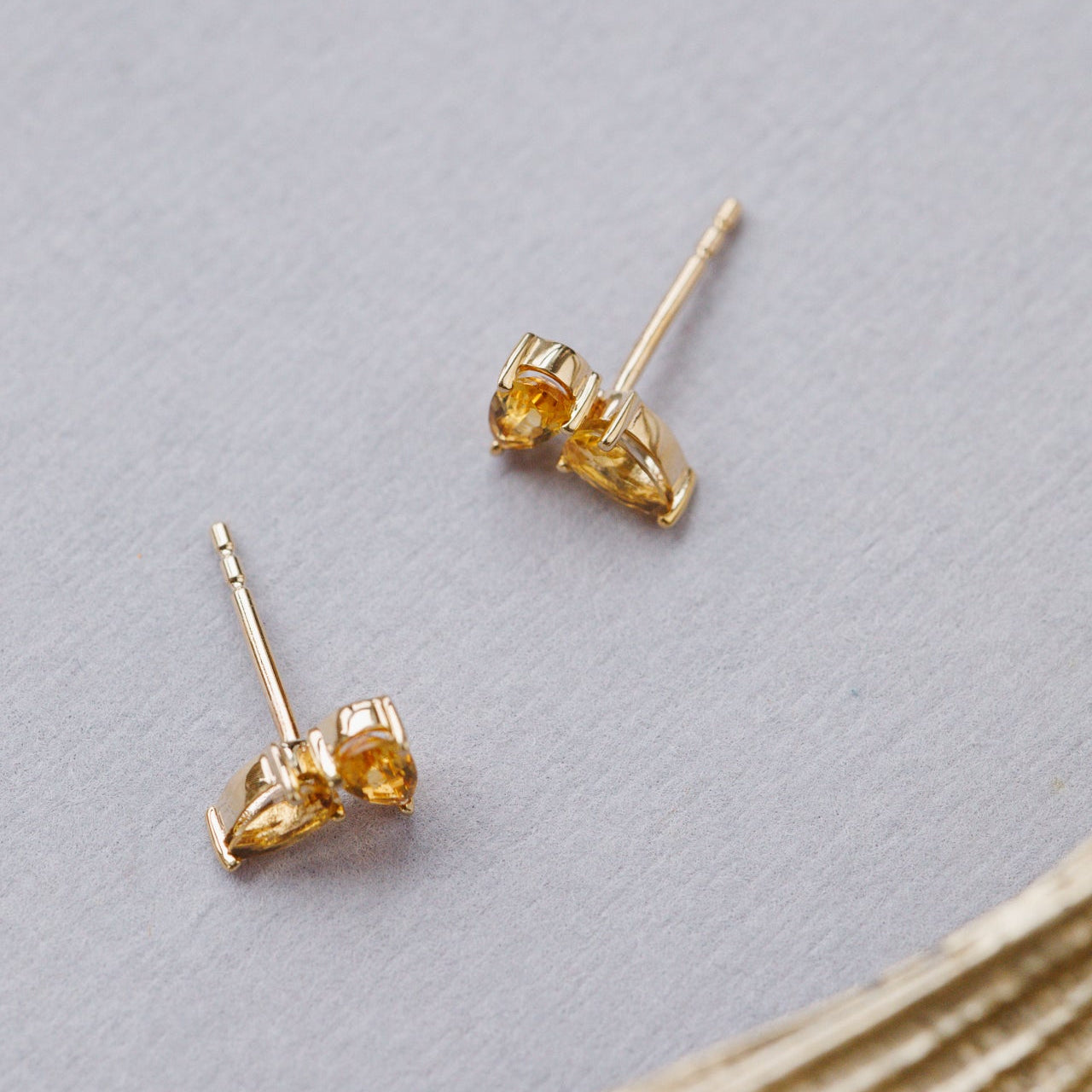 Gold earrings with citrine gemstones on a light gray background