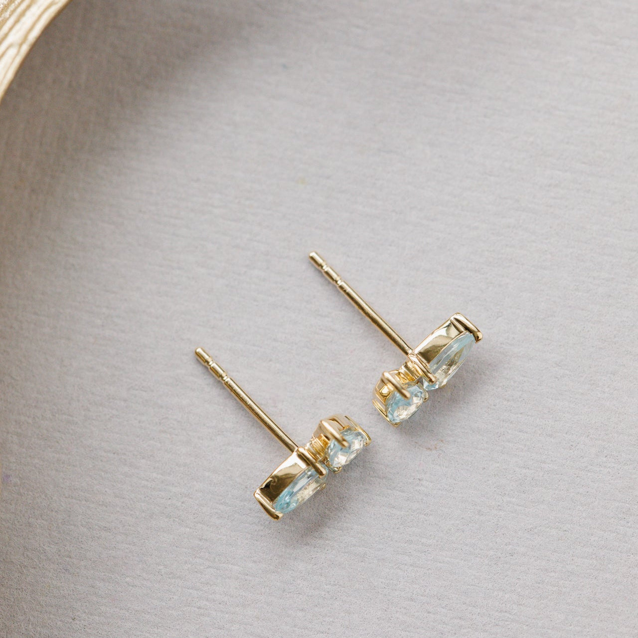 Gold earrings with blue topaz gemstones on a light gray background