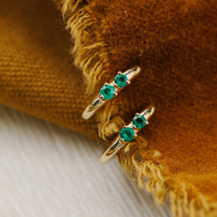 Gold earrings with green gemstones on a textured brown fabric background