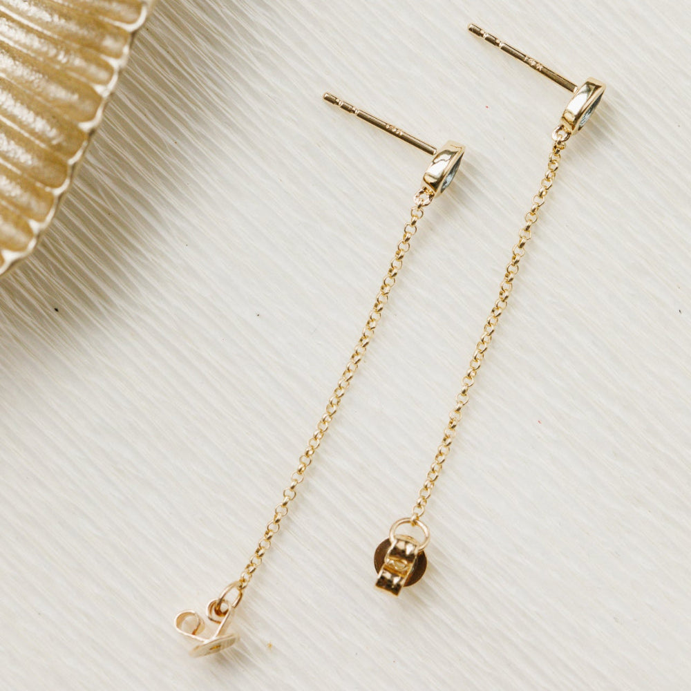 Gold chain earrings on a textured beige surface