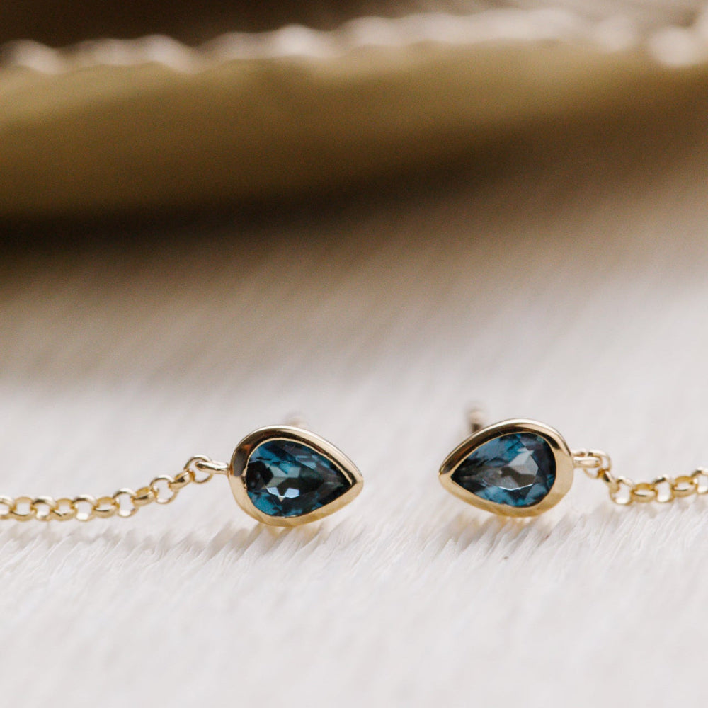 Gold bracelet with blue London blue topaz gemstones on a textured beige surface