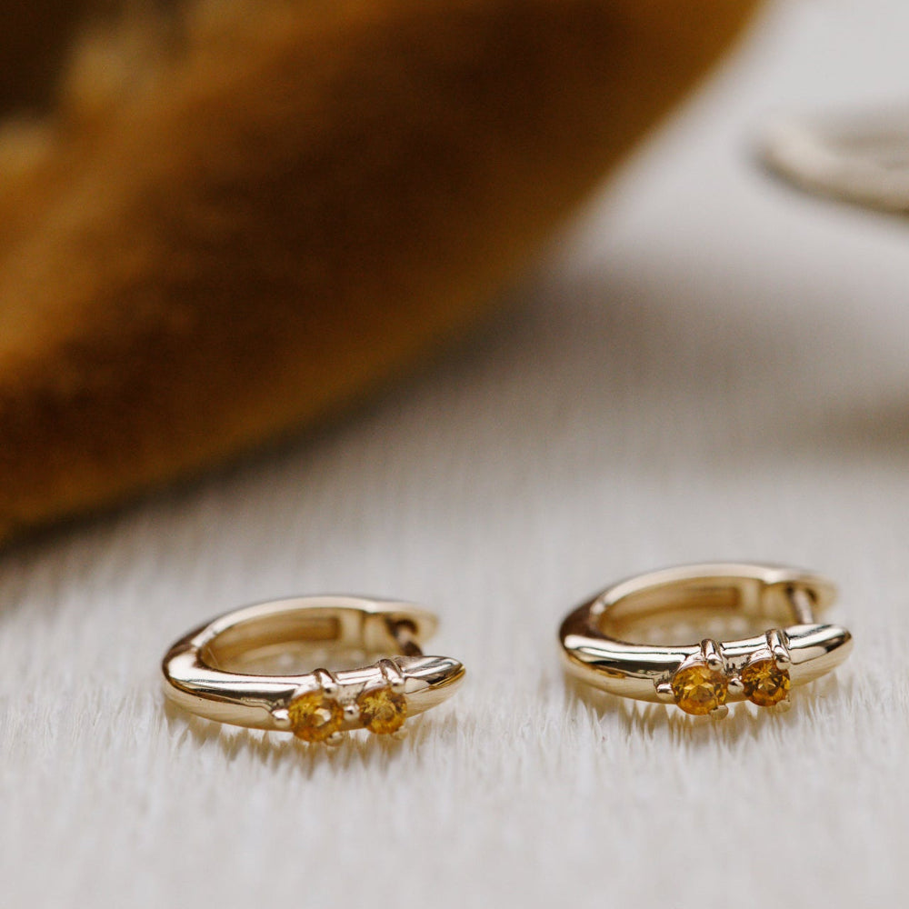 Gold hoop earrings with embedded yellow gemstones on a light wooden surface.