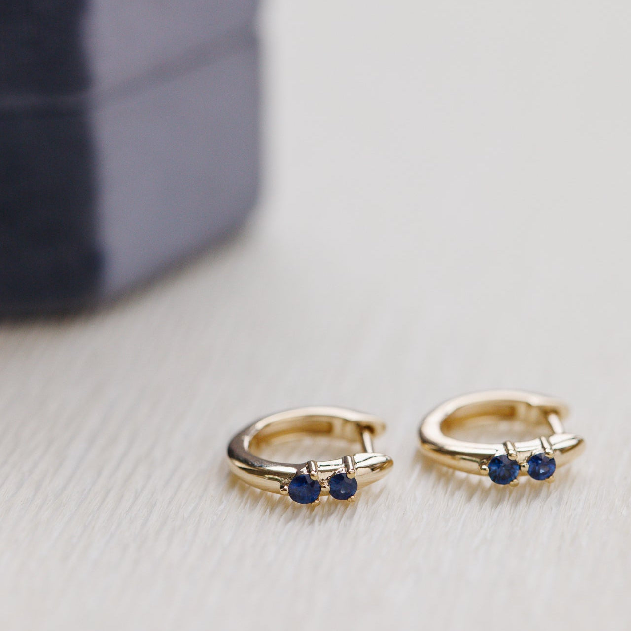 Gold hoop earrings with blue gemstones on a light gray surface.