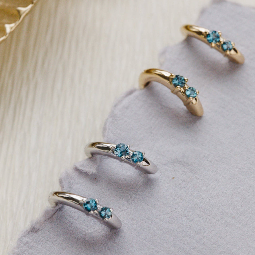 Yellow and white gold earrings with blue topaz gemstones on a textured surface