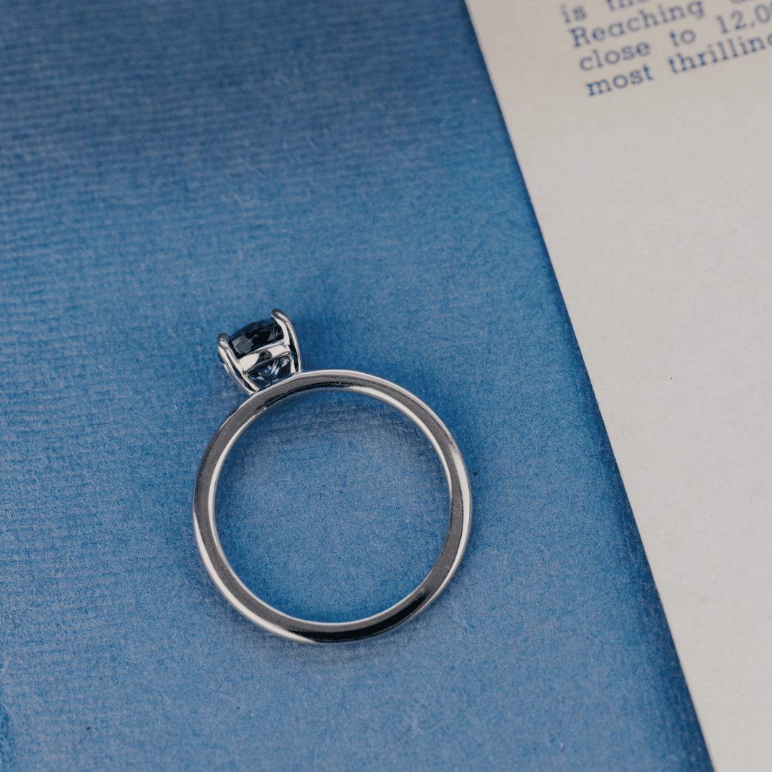 A 14k gold ring featuring a blue sapphire gemstone viewed from the top, displayed on a textured blue surface.