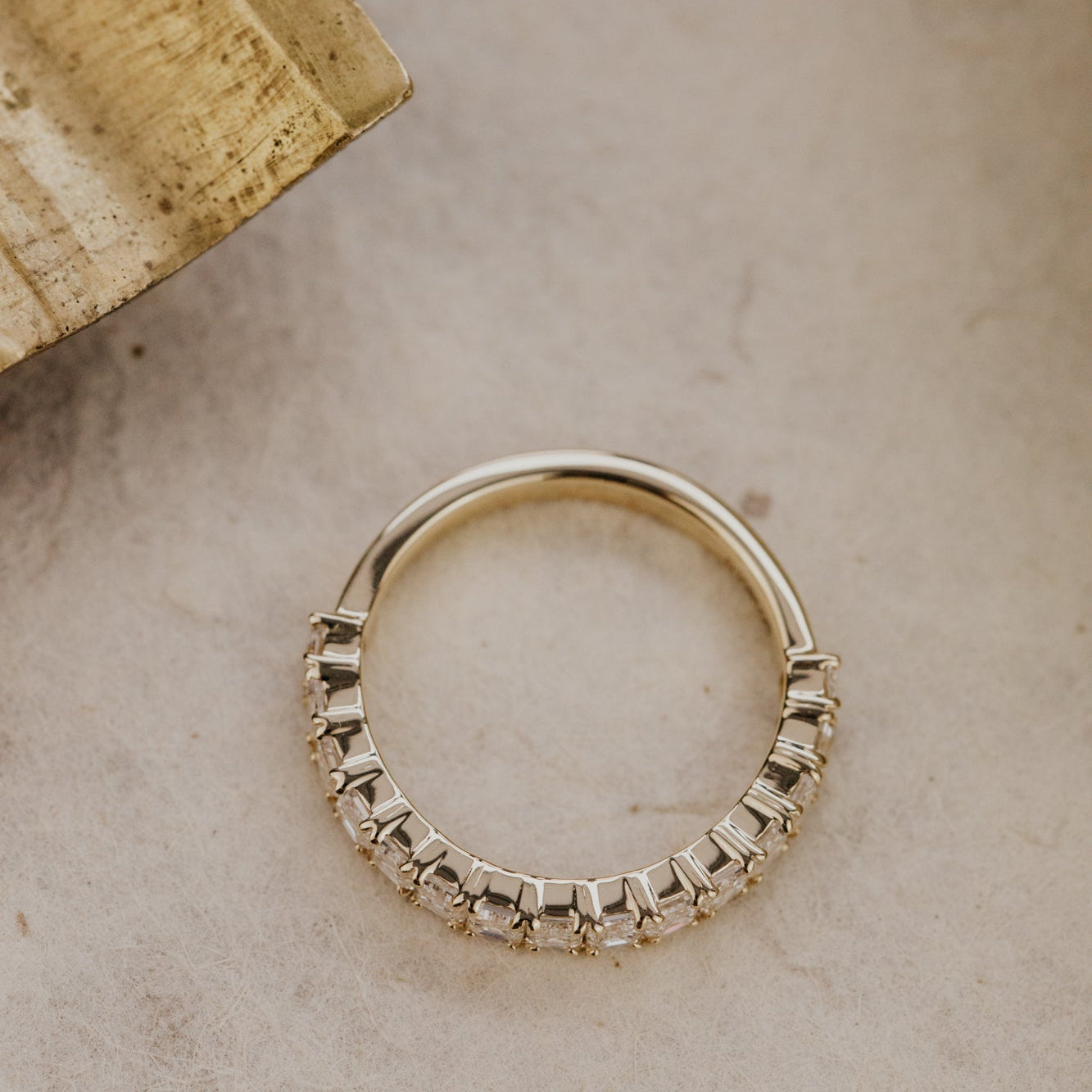 Top-down shot of the Mini Amara emerald cut diamond band in 14k yellow gold on a grey marbled surface.