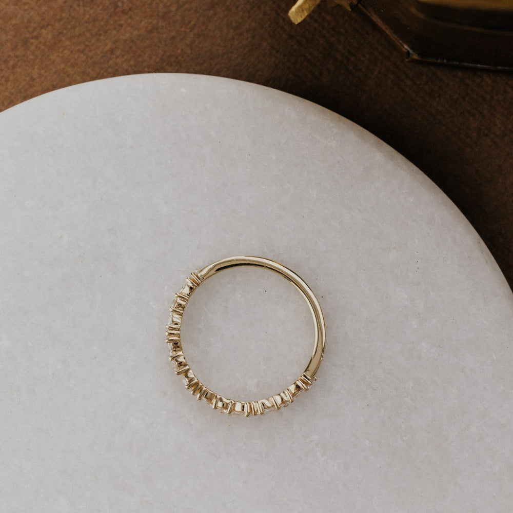 Gold wedding band on a white stone surface with a brown background.