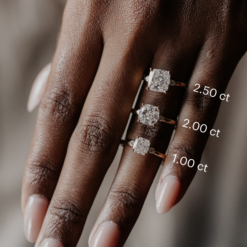 Three cushion-cut diamond engagement rings on a hand with labeled carat weights.