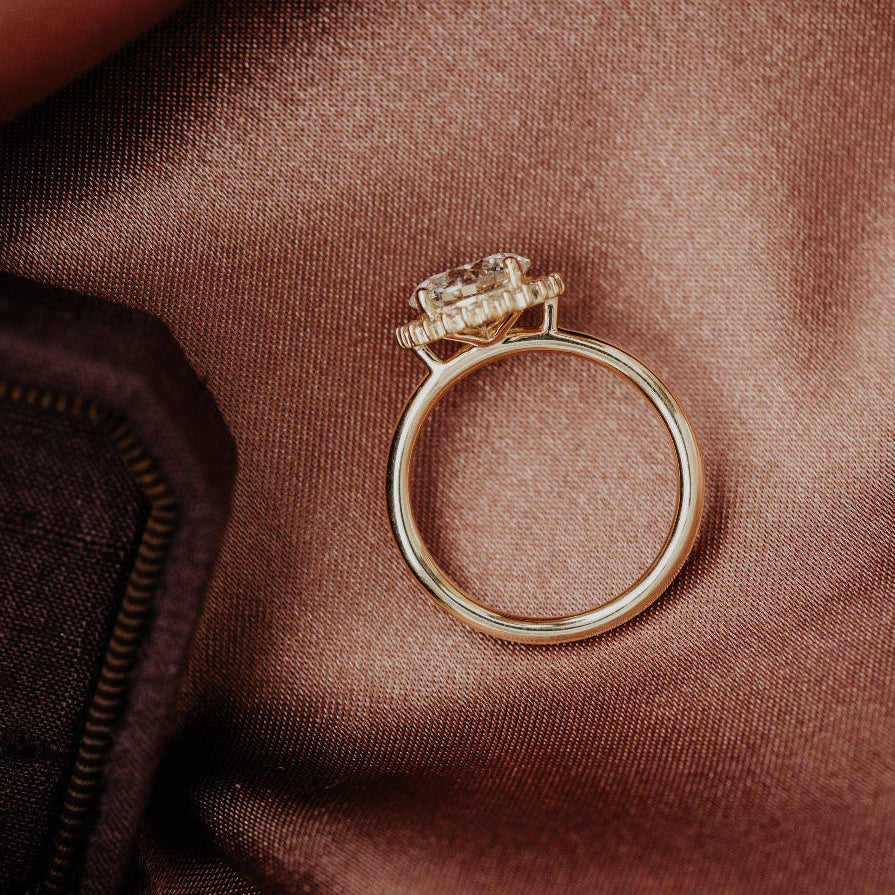 Gold engagement ring with a diamond on a brown fabric background