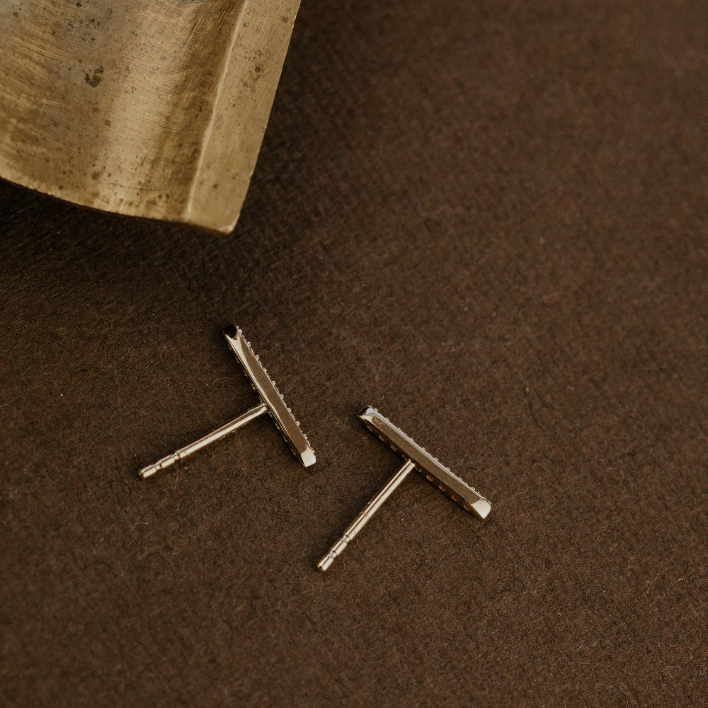Two long bar diamond earrings on a brown surface.