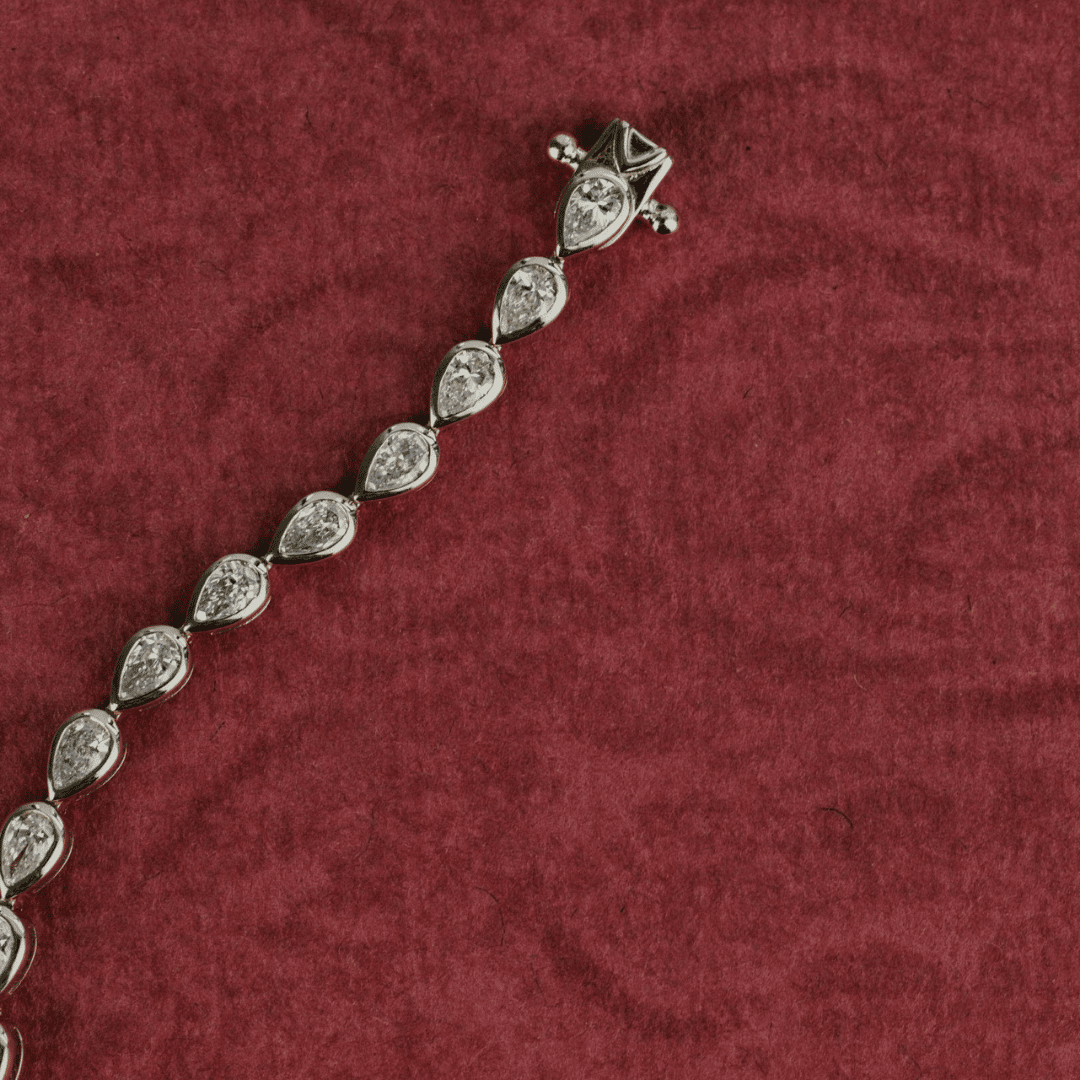 14k gold pear cut, lab grown diamond tennis bracelet featured on a textured red surface.