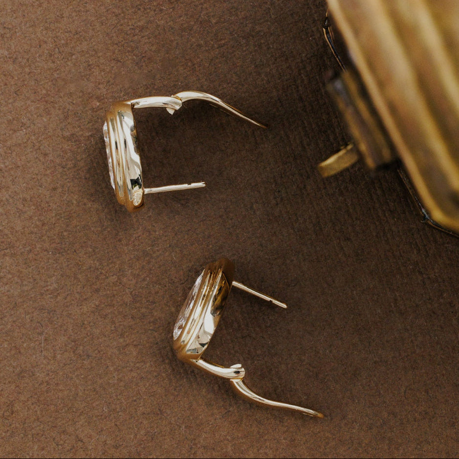 Gold pear shaped lab grown diamond earrings on a brown surface.