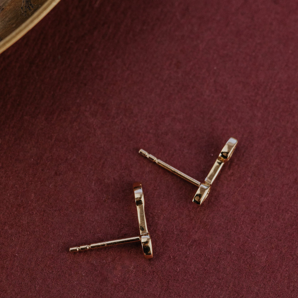 Gold earring posts on a maroon fabric background.