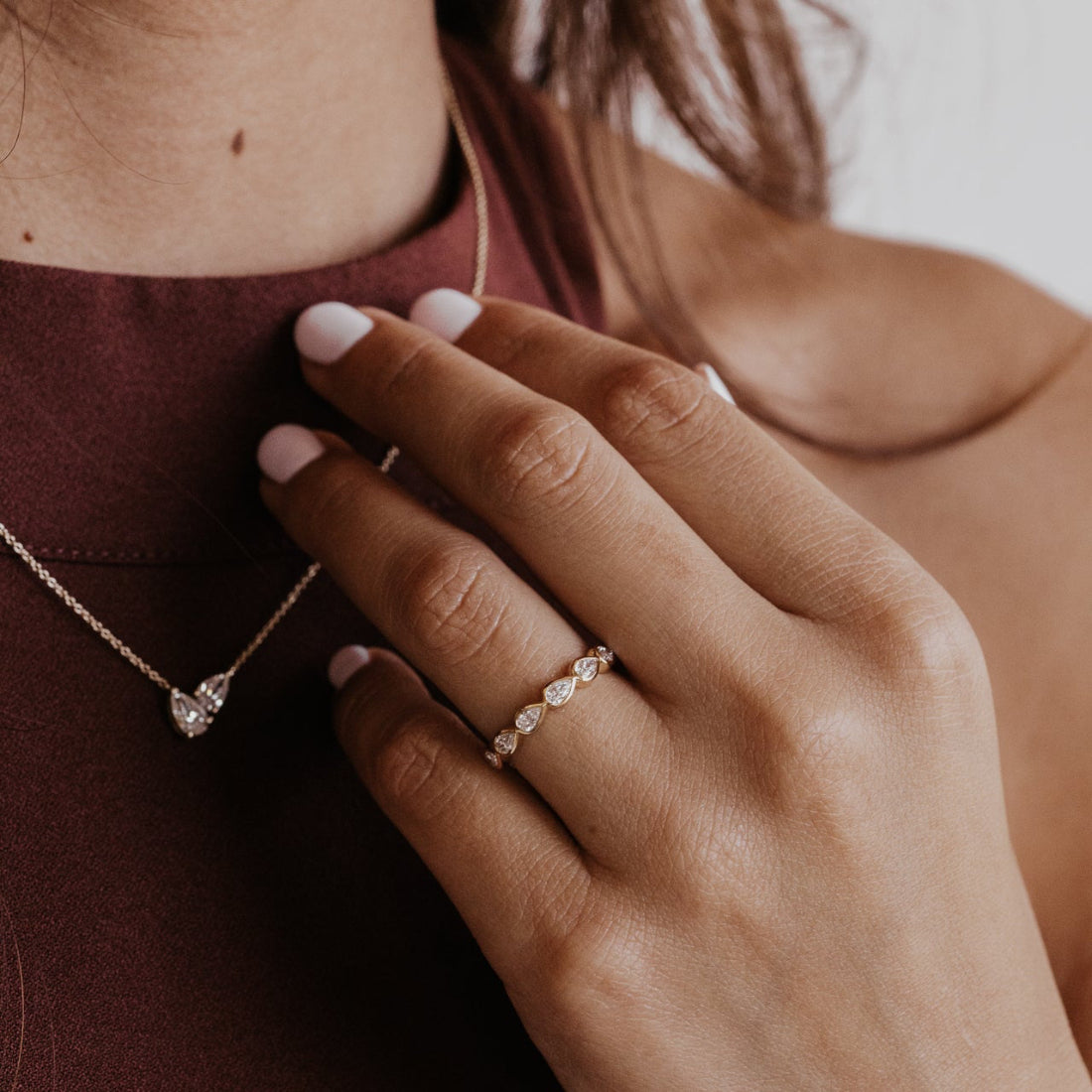 Close-up of a hand wearing a diamond wedding band with a diamond necklace, on a blurred background