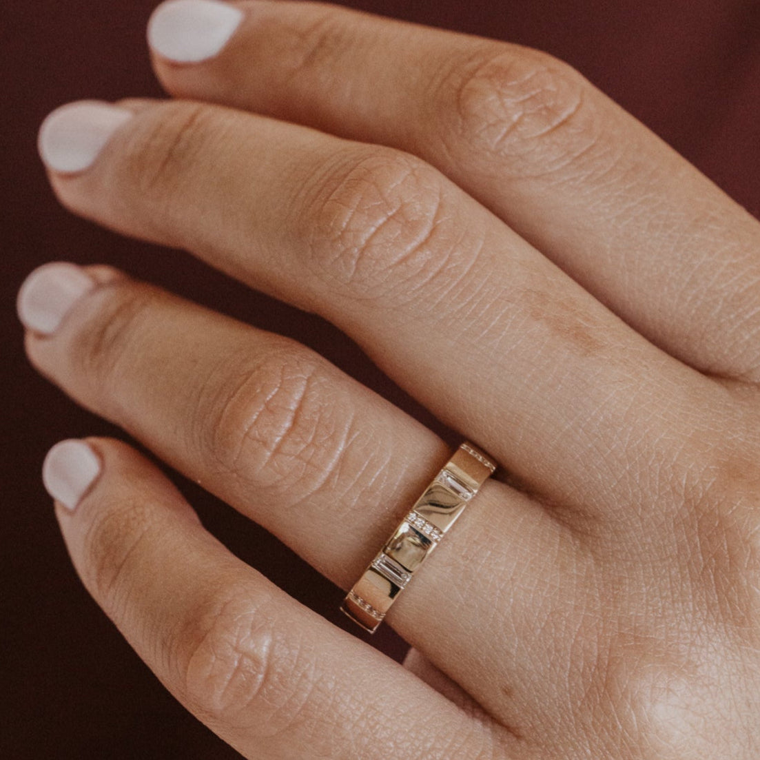 Hand wearing a gold wedding band with diamond accents on a dark background