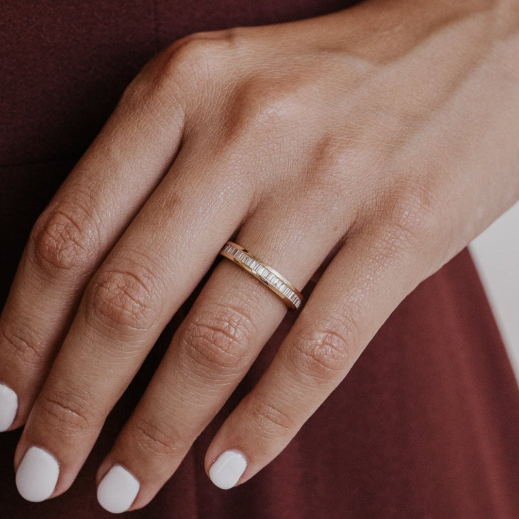 Close-up of a hand wearing a gold wedding band with natural diamonds on a blurred background