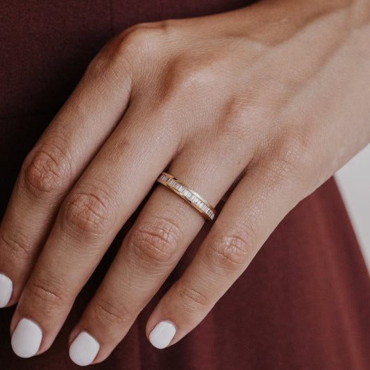 Close-up of a hand wearing a gold wedding band with natural diamonds on a blurred background