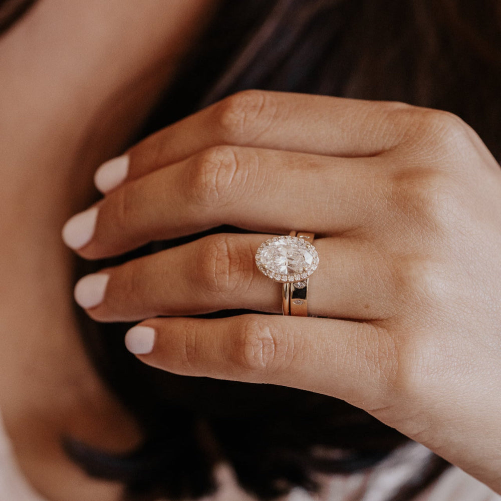 Close-up of a hand wearing a diamond engagement ring with a gold wedding band with marquise diamonds on blurred background