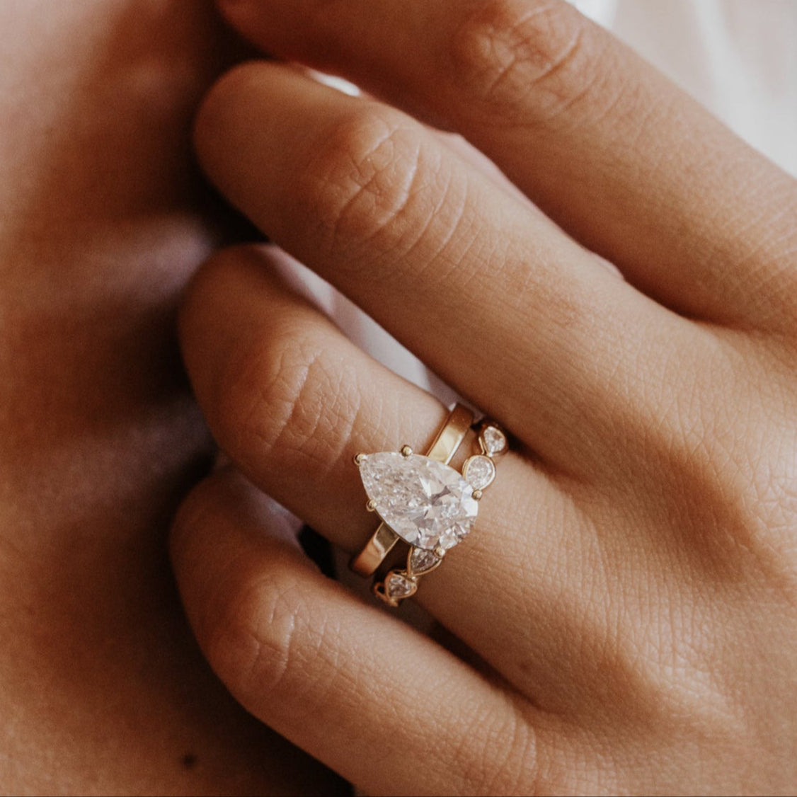 Close-up of a hand wearing a pear diamond ring with a soft focus background