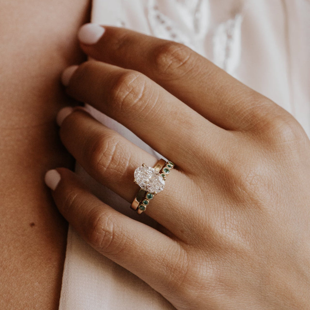 Close-up of a hand wearing an oval engagement ring with a blurred background