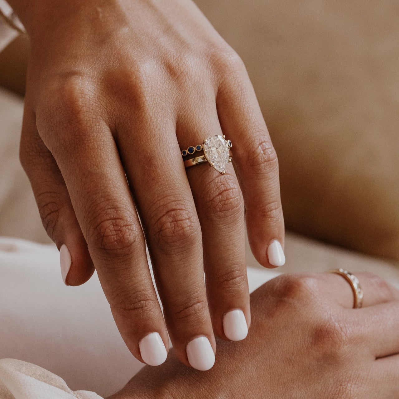 Close-up of a hand wearing a pear engagement ring with a blue sapphire band blurred background