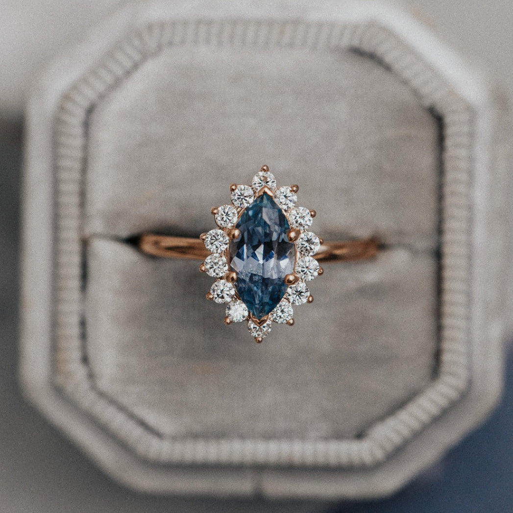 Ring with a blue gemstone and rose gold setting on a gray cushion