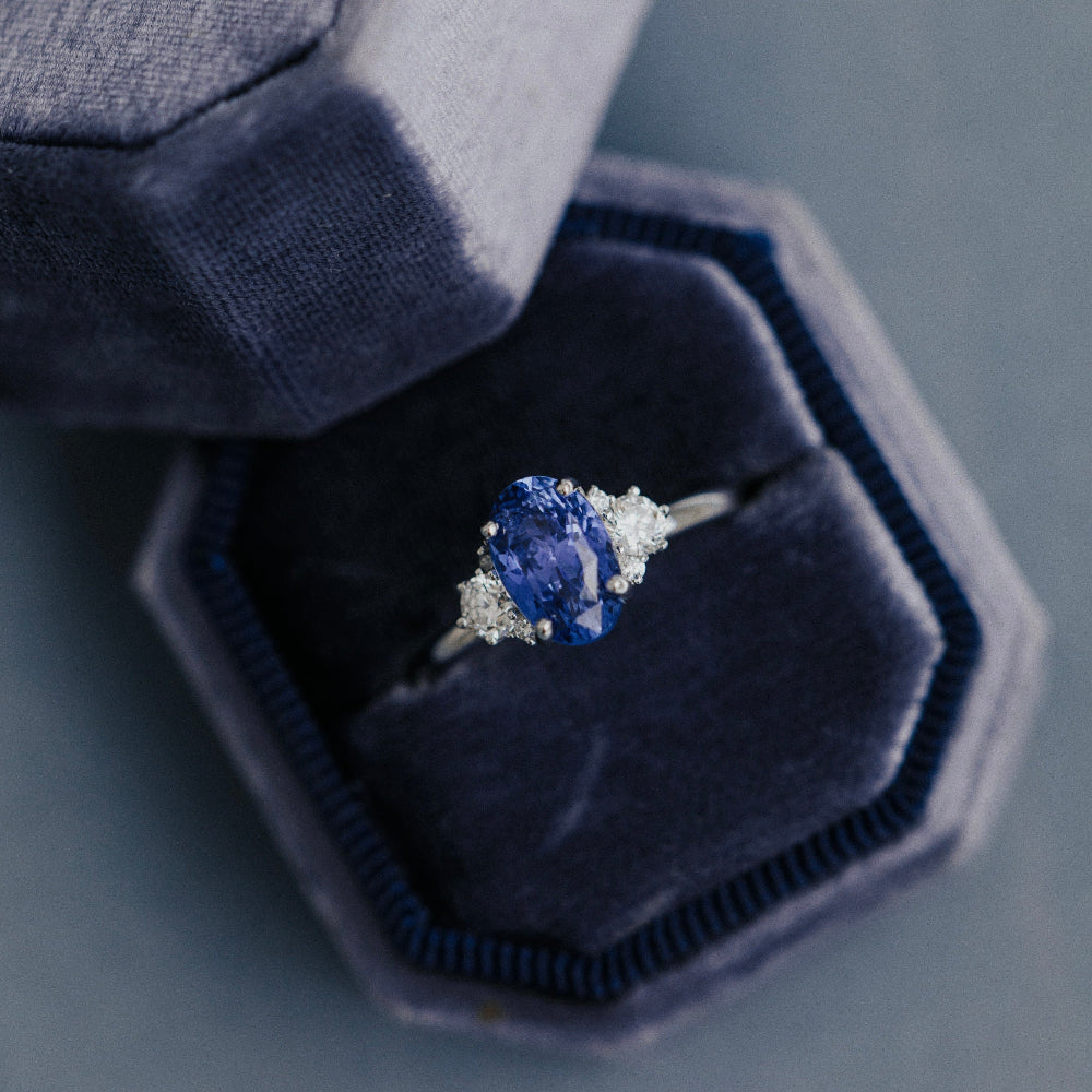 Ring with a blue sapphire in a hexagonal velvet box on a gray background
