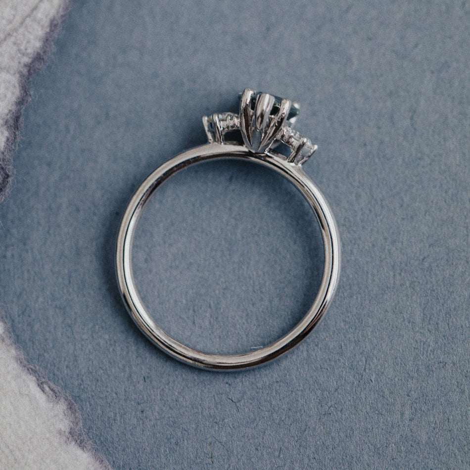 White gold ring with a diamonds and a sapphire center stone on a textured blue surface