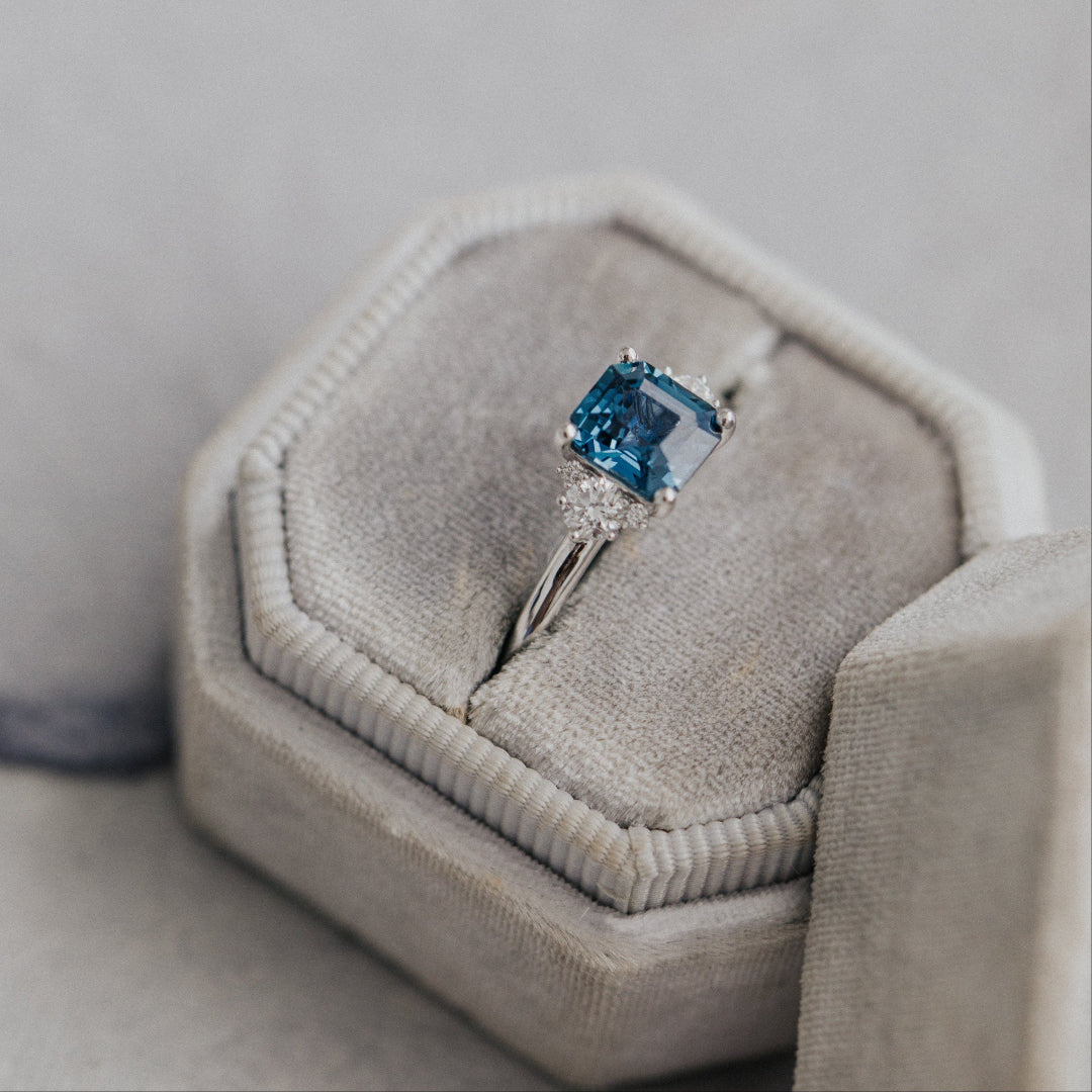 Ring with a blue Montana sapphire in a gray jewelry box on a light gray background