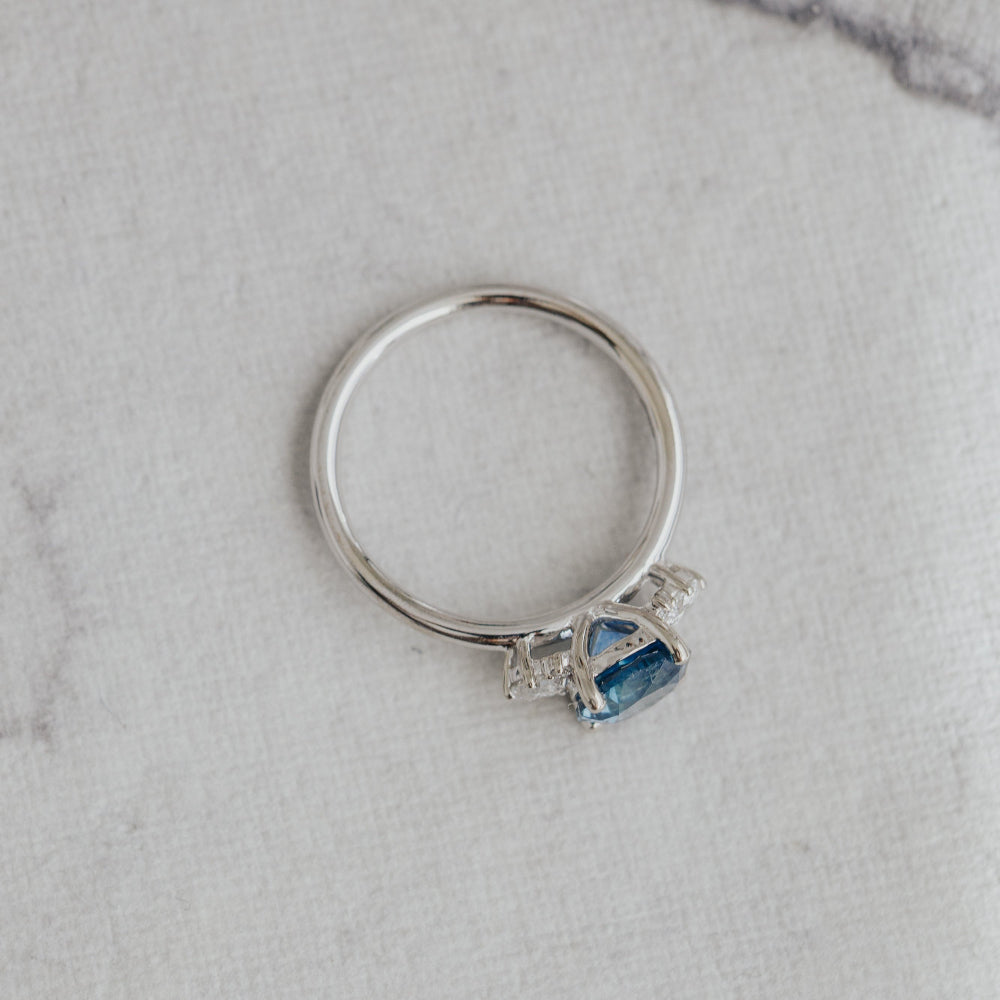 White gold ring with a blue Montana Sapphire on a gray marble surface