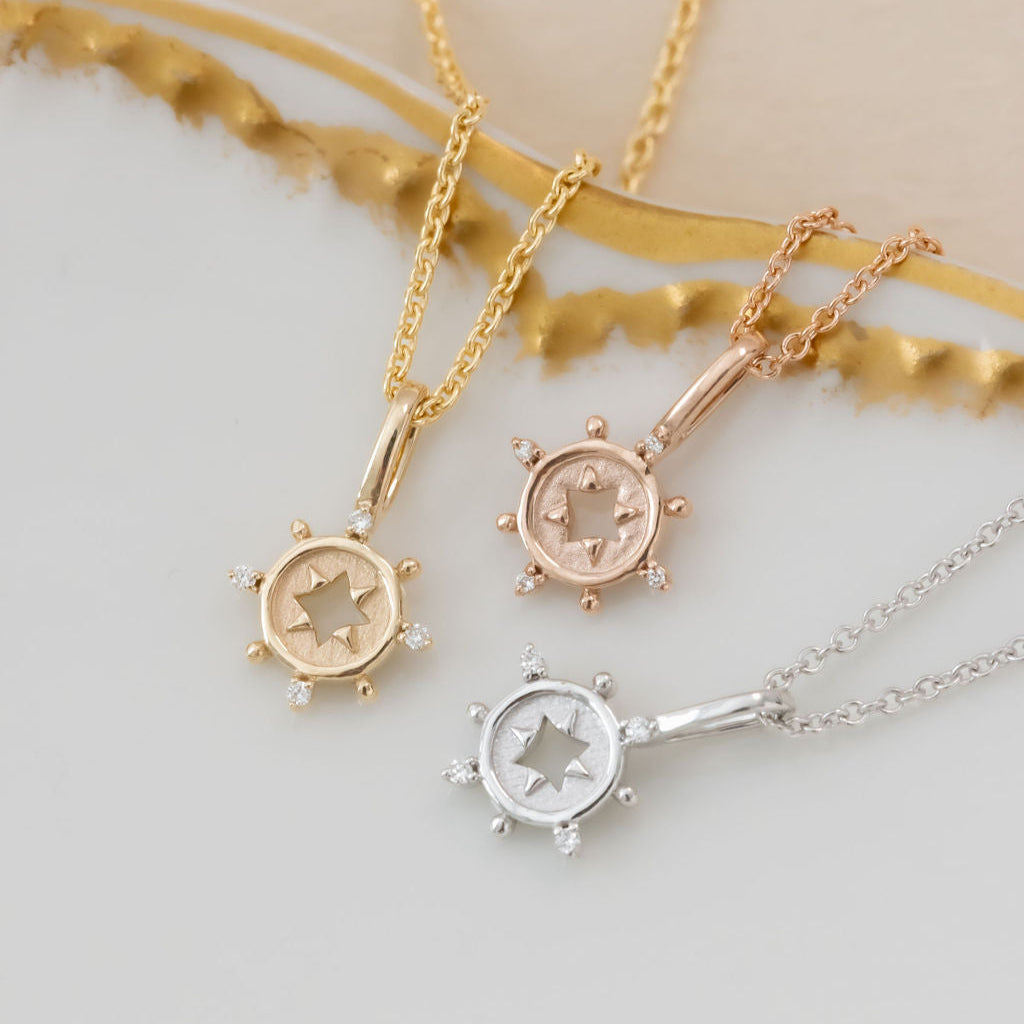 A collection of Mini Odyssey Necklaces with gold pendants and diamonds, displayed on a white surface.