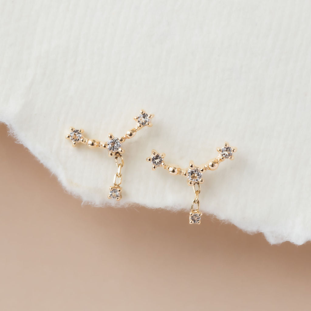 A pair of white topaz curved bar dangle earrings in 14k yellow gold, displayed against a neutral background.