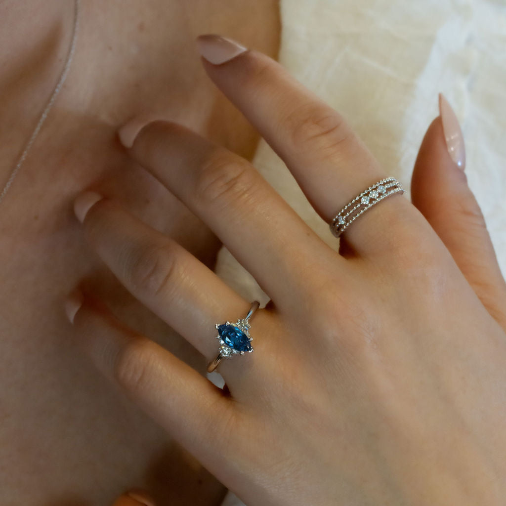 Close-up of a hand model wearing a ring with a blue sapphire and diamond accents.