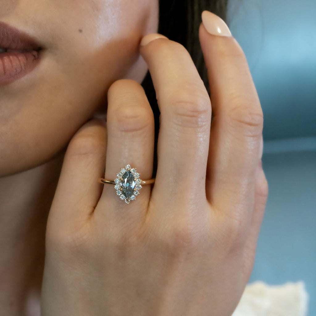 Close-up of a hand wearing a ring with a blue sapphire gemstone against a blurred background
