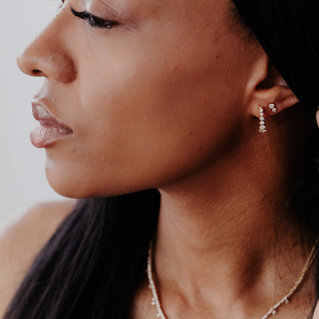 Close-up of a woman wearing earrings and a necklace against a neutral background