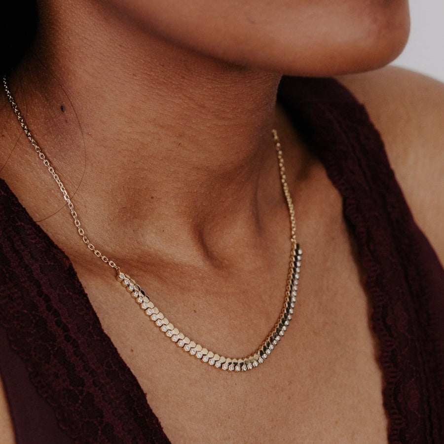Close-up of a person wearing a delicate gold diamond necklace against a neutral background