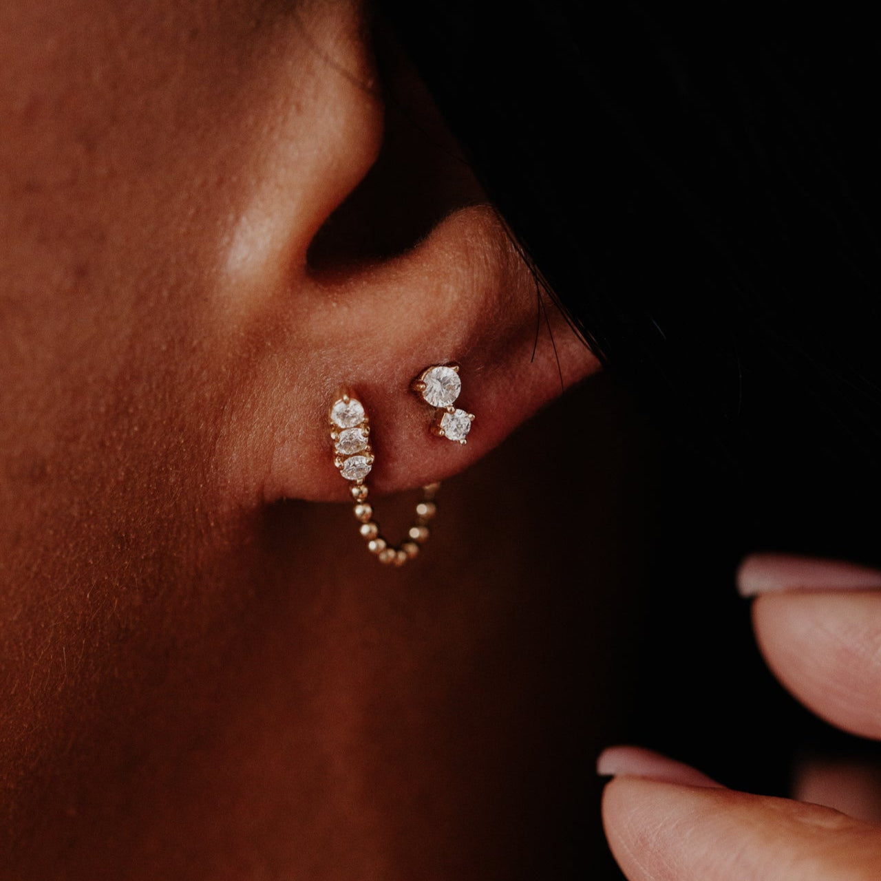 Close-up of a person wearing diamond stud earrings with a dark background