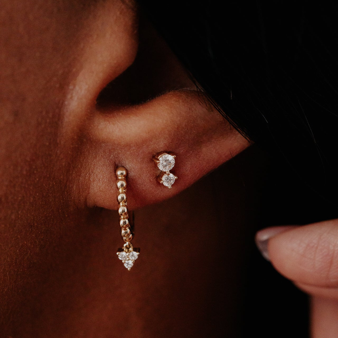 Close-up of an ear with gold and diamond earrings against a dark background