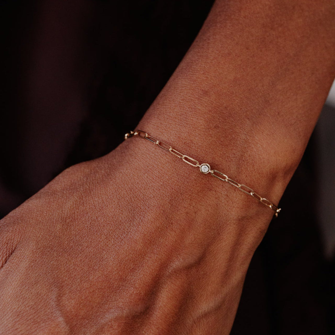 Gold chain bracelet with a small diamond on a wrist against a dark background