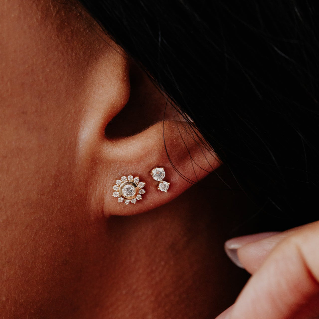 Close-up of an ear wearing two diamond earrings with a blurred background