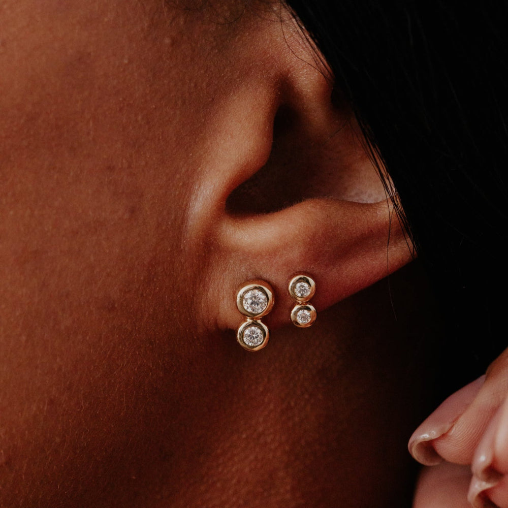 Close-up of an ear wearing gold earrings with diamonds against a dark background