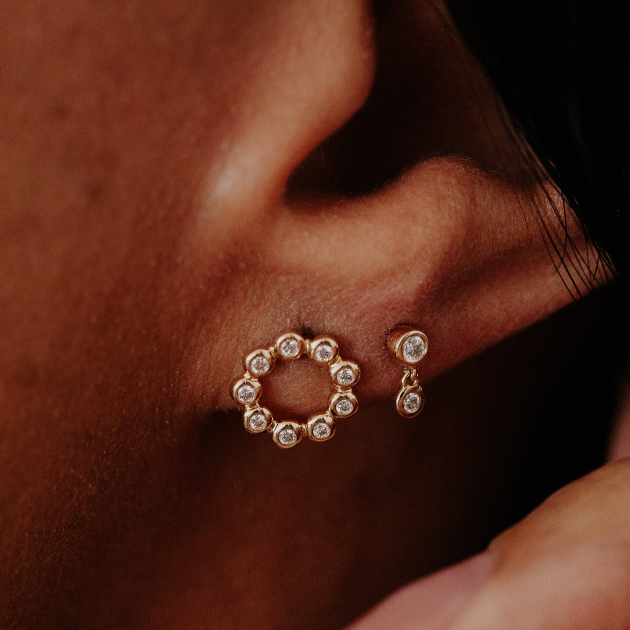 Close-up of gold round stud earrings with gemstones on an ear.