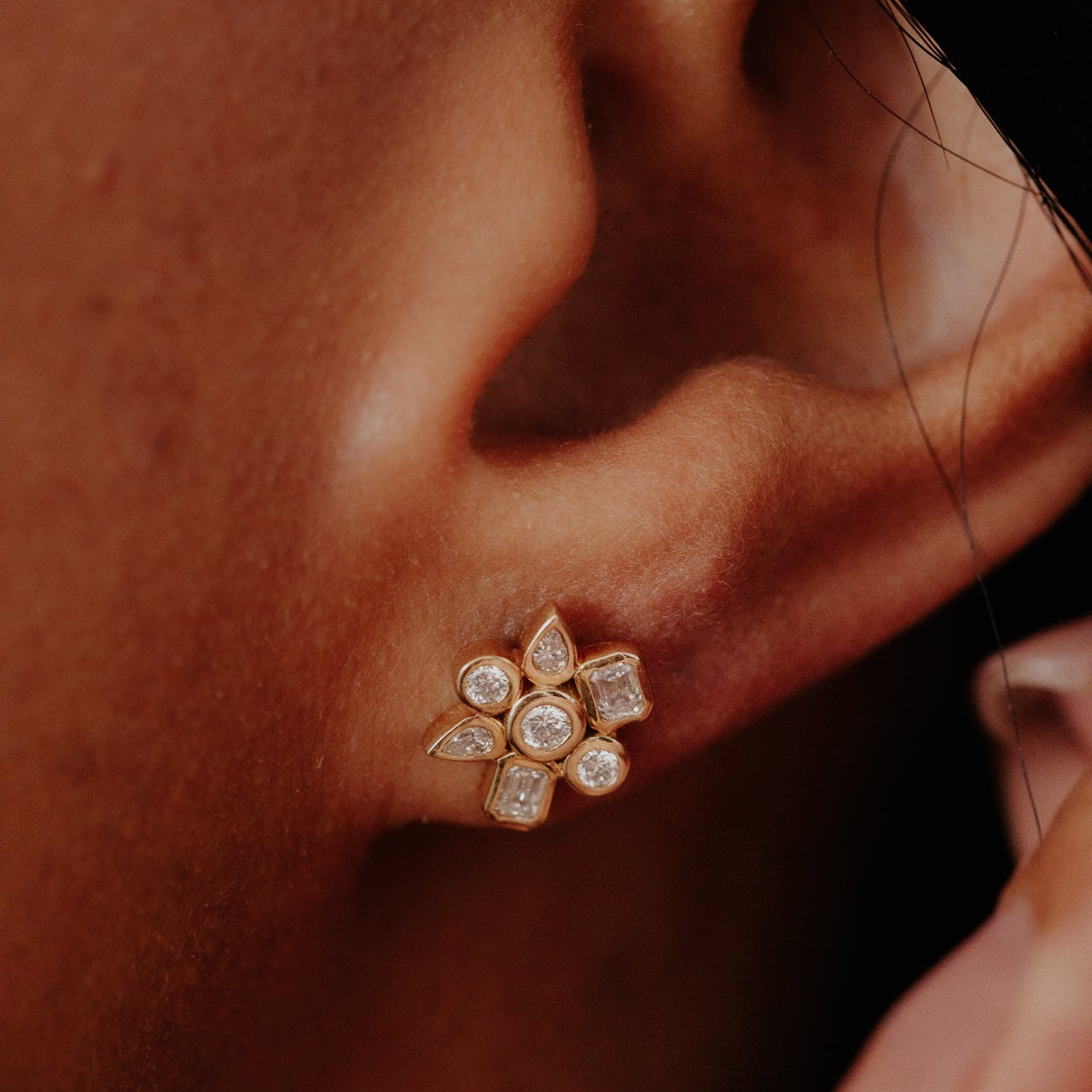 Close-up of a diamond earring worn on an ear against a dark background