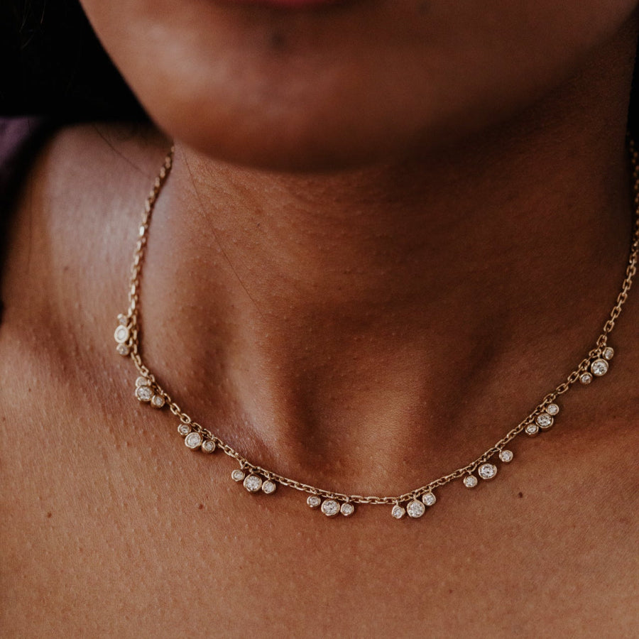Close-up of a person wearing a delicate gold necklace with diamond clusters